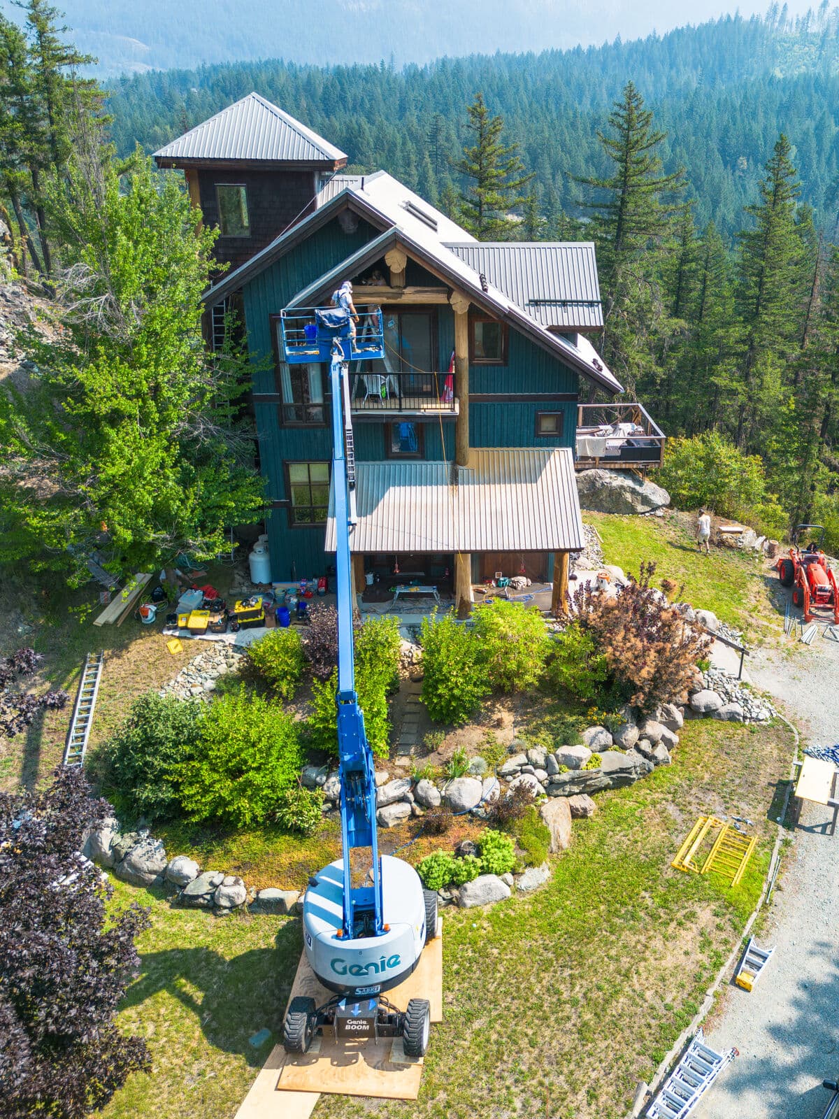 Drone view of a three-storey teal board-and-batten mountain home with metal roof and log posts