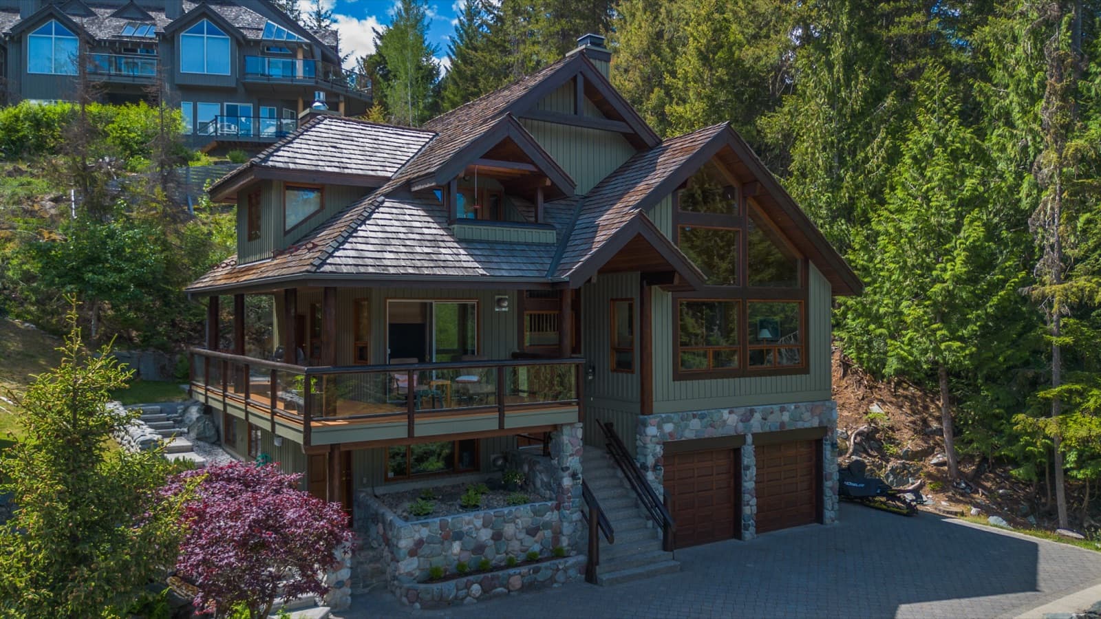 Drone view of a sage-green board-and-batten chalet with dark timber trim, cedar shake roof