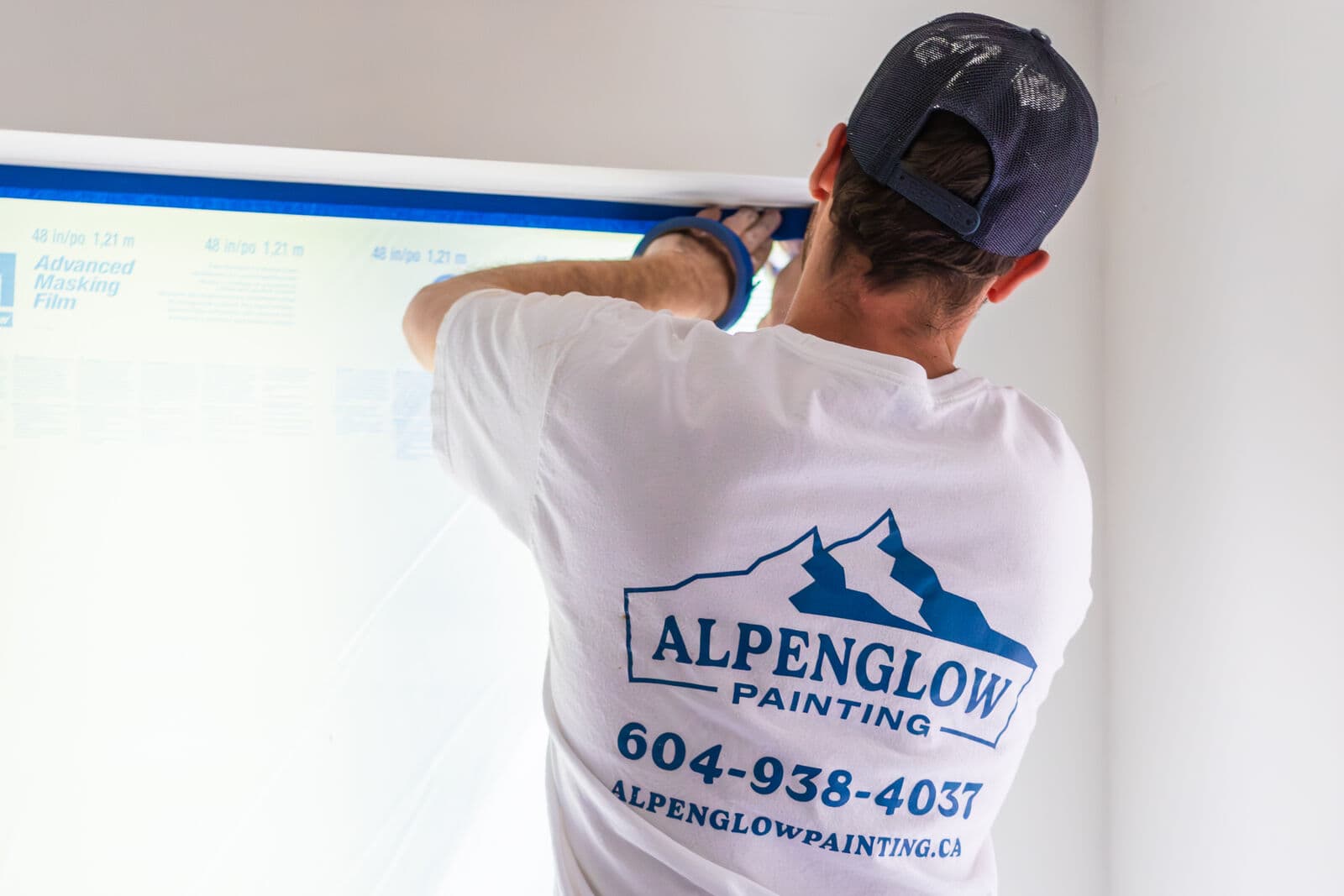 Painter in a navy trucker cap and white Alpenglow Painting t-shirt with large logo, phone number