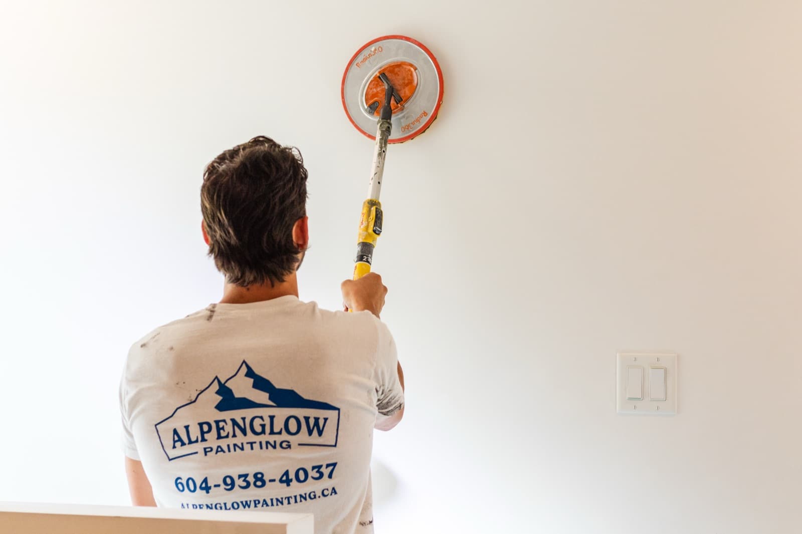 Wider view of a painter pole-sanding a white interior wall with a Radius 360 sander