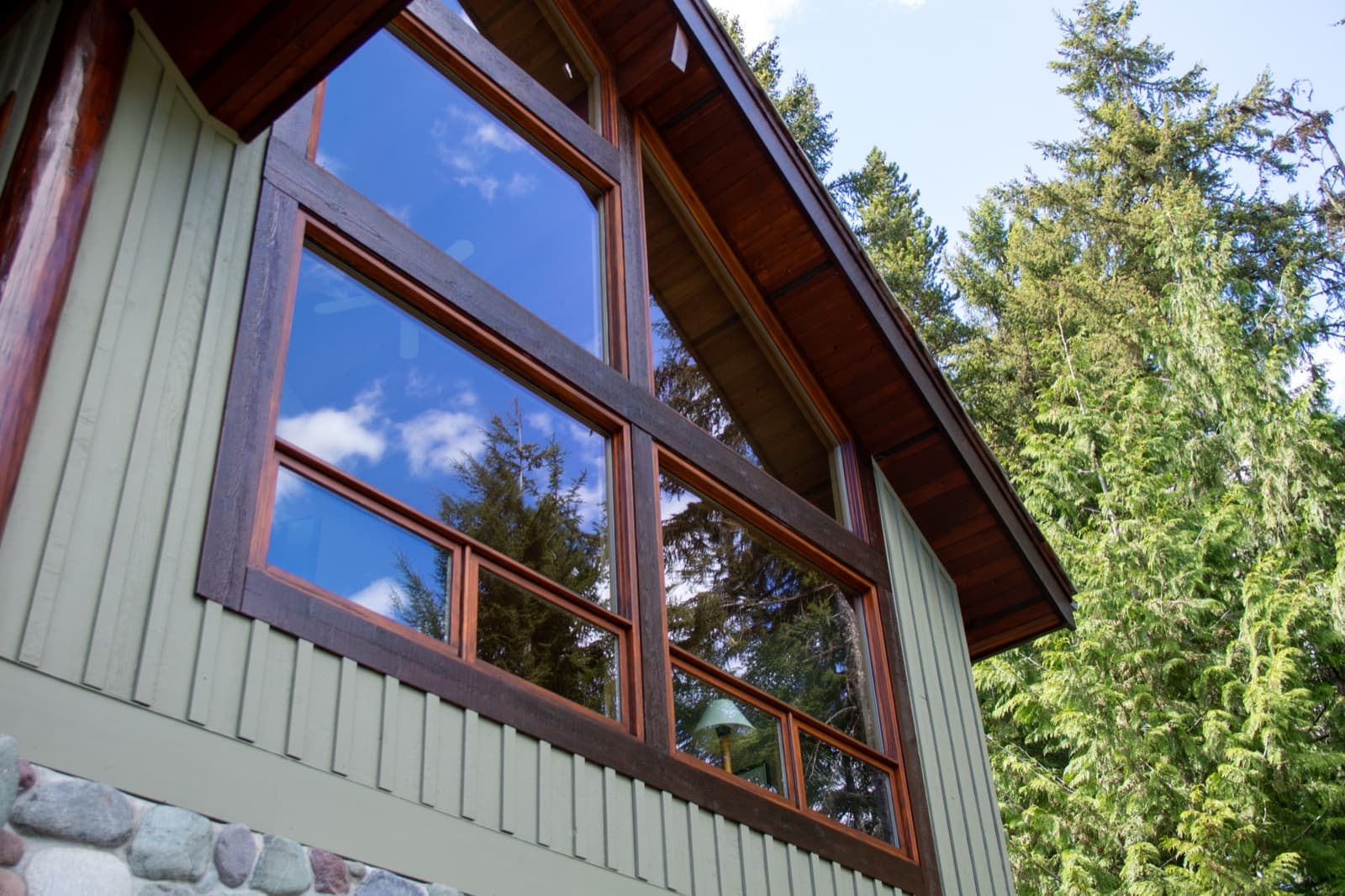 Low-angle view of the same chalet's gable-end window wall showing dark-stained timber frames with orange cedar sashes reflecting blue sky