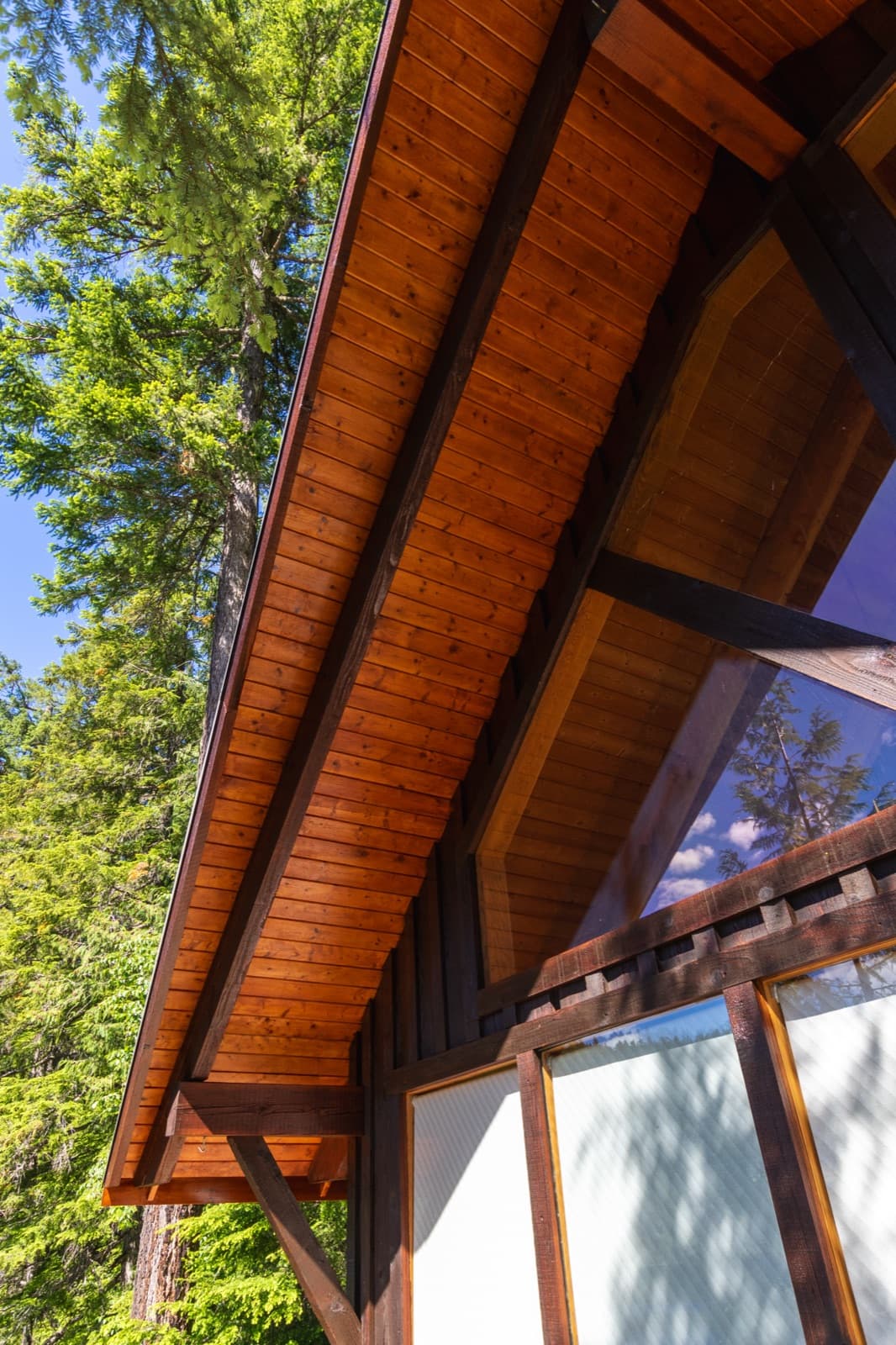 Upward portrait view along a chalet roofline showing refinished orange cedar plank soffits and dark espresso timber beams against blue sky