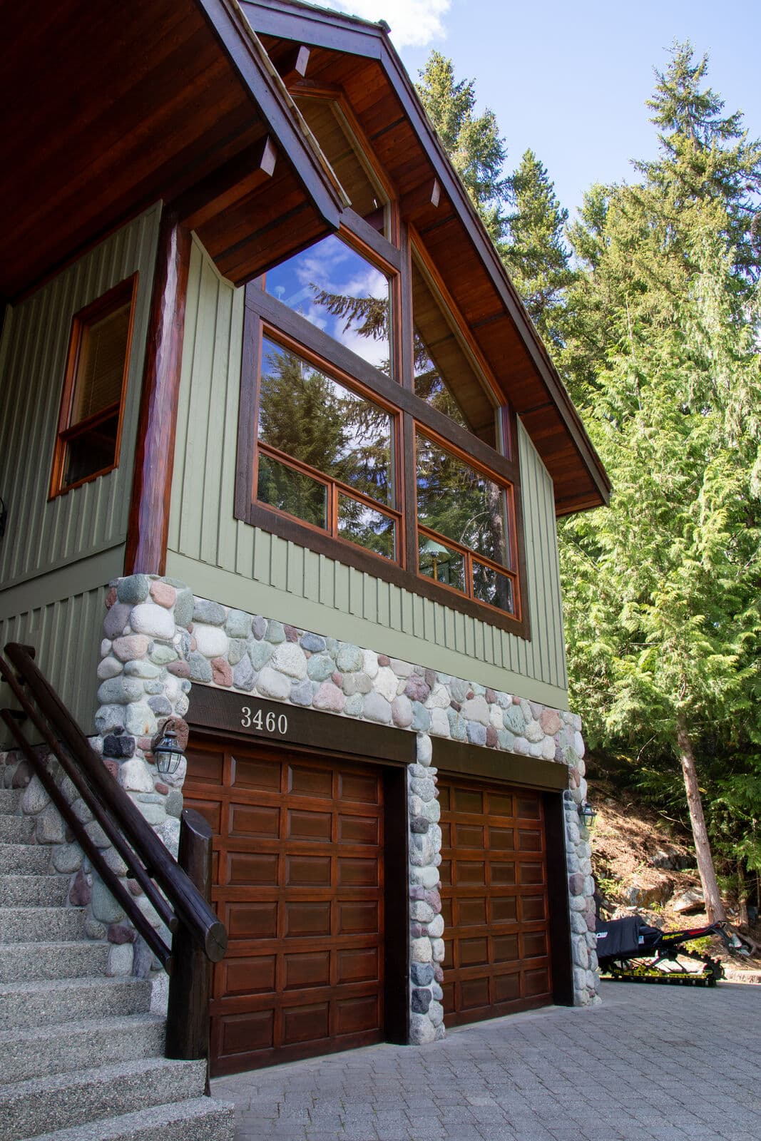 Full exterior view of a Whistler chalet with freshly painted sage green board-and-batten siding, dark espresso-stained trim and log posts