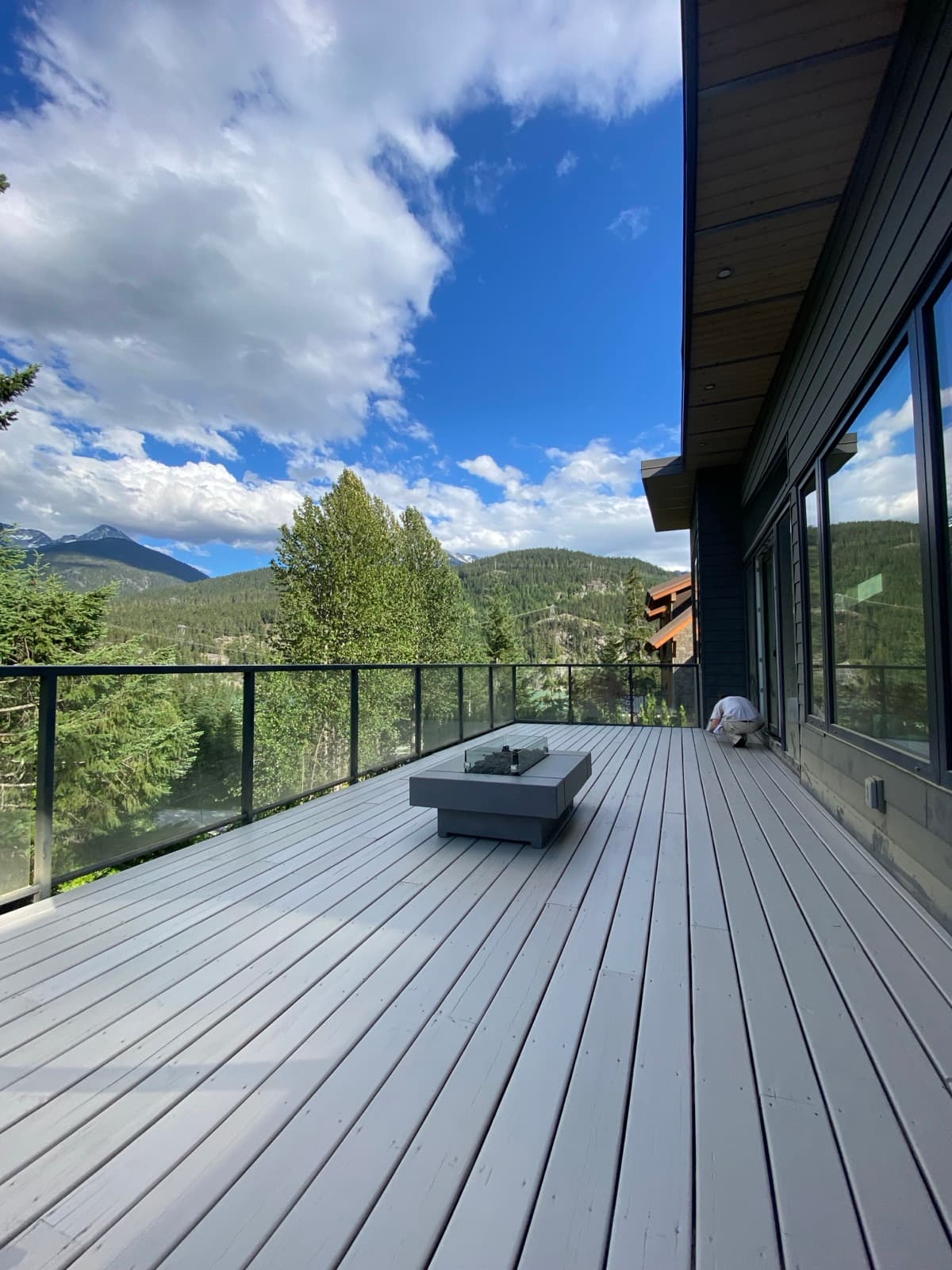 Upward angle of freshly painted light grey horizontal lap siding on a modern home with a glass-panel deck railing, black metal window box