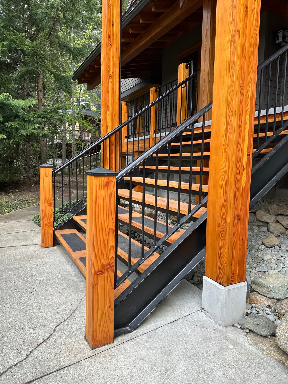 Richly stained Douglas fir posts and beams framing a black steel exterior staircase with flat-bar metal railings